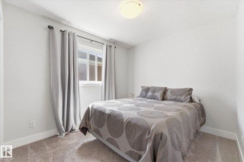 Carpeted bedroom featuring white walls, a white trim baseboard, a ceiling-mounted flush light fixture, and a window with a white frame and dark curtain rod - 54 Cypress Link, Fort Saskatchewan, AB - Indoor Photo Showing Bedroom