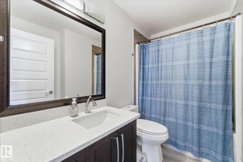 Bathroom featuring a dark wood-framed mirror, light-toned countertop, integrated sink, and dark wood-finish cabinetry - 54 Cypress Link, Fort Saskatchewan, AB - Indoor Photo Showing Bathroom