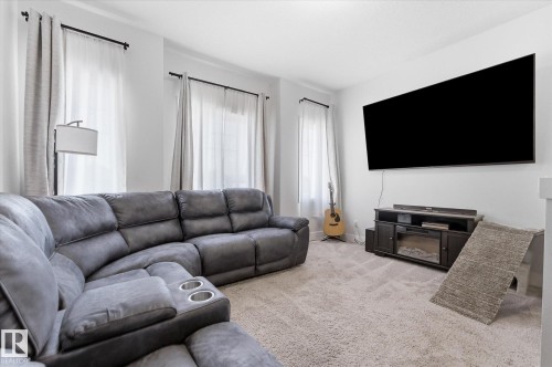 Carpeted living area featuring a wall-mounted television, recessed lighting, crown molding, and multiple windows with curtain rods - 54 Cypress Link, Fort Saskatchewan, AB - Indoor Photo Showing Living Room