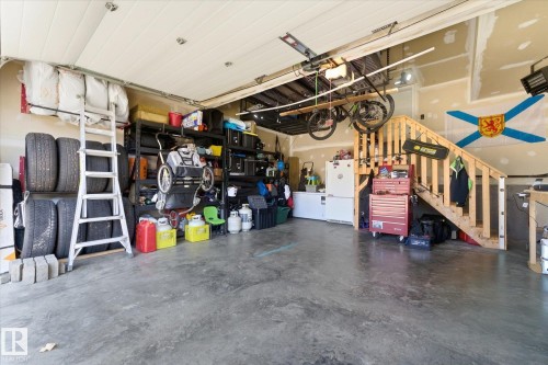 Concrete flooring garage space featuring an overhead door, exposed wood staircase, and interior wall finish - 54 Cypress Link, Fort Saskatchewan, AB - Indoor Photo Showing Garage