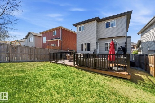 Expansive fenced backyard featuring a manicured lawn, a two-story gray siding exterior, and a wooden deck with black railing - 54 Cypress Link, Fort Saskatchewan, AB - Outdoor With Deck Patio Veranda With Exterior