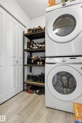 Stacked washer and dryer units, wood-finish flooring, and white bi-fold doors - 9 850 Secord Boulevard, Edmonton, AB - Indoor Photo Showing Laundry Room