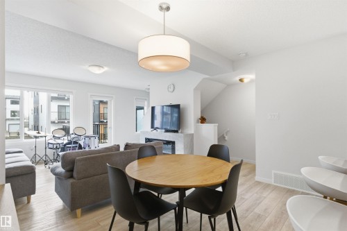 Open-concept living space featuring wood-finish flooring, a modern fireplace, multiple windows for ample natural light, and a contemporary drum pendant light fixture - 9 850 Secord Boulevard, Edmonton, AB - Indoor Photo Showing Dining Room