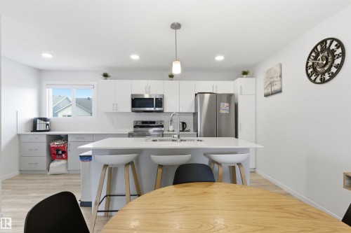 Modern kitchen featuring white cabinetry, stainless steel appliances, a center island with bar seating, a tile backsplash, and recessed lighting - 9 850 Secord Boulevard, Edmonton, AB - Indoor