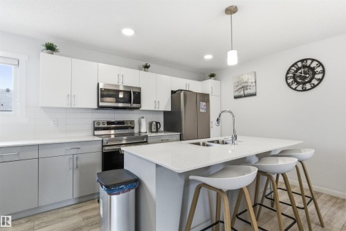 Modern kitchen featuring a central island with integrated double-basin sink and bar seating - 9 850 Secord Boulevard, Edmonton, AB - Indoor Photo Showing Kitchen With Double Sink With Upgraded Kitchen