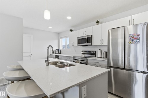 Modern kitchen featuring a large island with an undermount double sink, chrome gooseneck faucet, light-toned countertop, and recessed lighting - 9 850 Secord Boulevard, Edmonton, AB - Indoor Photo Showing Kitchen With Double Sink With Upgraded Kitchen
