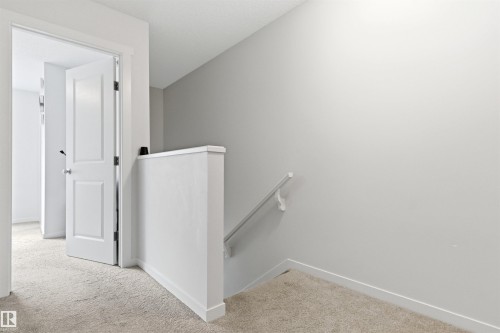 Upper-level hallway with neutral carpet flooring, light gray wall paint, white trim, and a white paneled door - 9 850 Secord Boulevard, Edmonton, AB - Indoor Photo Showing Other Room