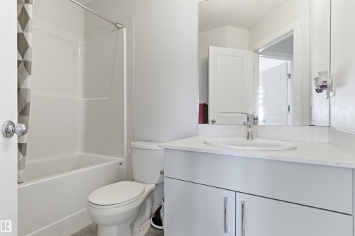 Bathroom featuring a white integrated tub and shower unit, a toilet, a vanity with a white countertop, an undermount sink, and a chrome faucet - 9 850 Secord Boulevard, Edmonton, AB - Indoor Photo Showing Bathroom