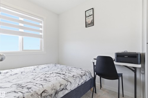 Bright interior space featuring a window with layered white shades, white walls, and light-colored carpeting - 9 850 Secord Boulevard, Edmonton, AB - Indoor Photo Showing Bedroom