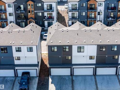 Townhome exteriors feature multi-tone siding, dark framed windows, and individual garages with white doors - 9 850 Secord Boulevard, Edmonton, AB - Outdoor With Facade