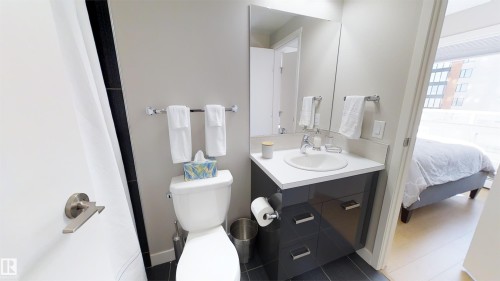 Bathroom featuring a white toilet, dark vanity with a white countertop and integrated sink, and a wall-mounted mirror - #1603 10410 102 Av Nw, Edmonton, AB - Indoor Photo Showing Bathroom