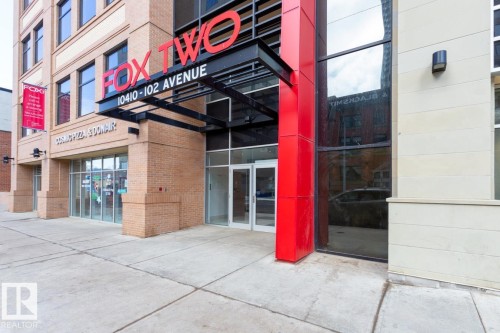 Modern building entrance featuring a prominent red architectural column and a large glass facade - #1603 10410 102 Av Nw, Edmonton, AB - Outdoor With Exterior