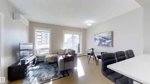 Open-concept living space featuring light wood-finish flooring, white walls, and a modern ceiling light fixture - #1603 10410 102 Av Nw, Edmonton, AB - Indoor