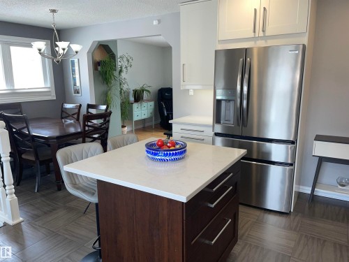 The kitchen features a center island with a light-colored countertop and dark wood cabinetry with chrome handles - 14212 30 Street, Edmonton, AB - Indoor