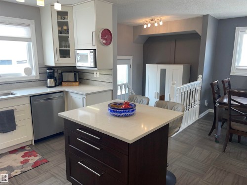The property features a kitchen with white cabinetry, a kitchen island with a light-colored countertop, and a stainless steel dishwasher - 14212 30 Street, Edmonton, AB - Indoor Photo Showing Other Room