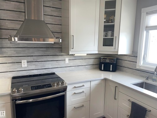 The kitchen features white cabinetry, a stainless steel range, a stainless steel range hood, light-colored countertops, and a tiled backsplash - 14212 30 Street, Edmonton, AB - Indoor Photo Showing Kitchen