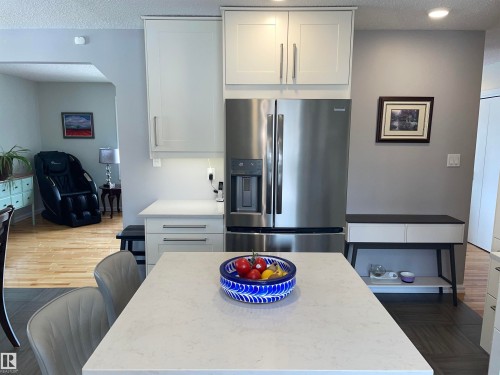 The kitchen features white cabinetry with stainless steel handles, a stainless steel refrigerator, and a light-colored countertop - 14212 30 Street, Edmonton, AB - Indoor