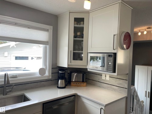 The kitchen features white cabinetry, a stainless steel sink with a modern faucet, and a light-colored countertop - 14212 30 Street, Edmonton, AB - Indoor Photo Showing Kitchen