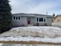 This property features a single-story structure with grey siding, a dark grey roof, and a vibrant red front door - 14212 30 Street, Edmonton, AB  - Outdoor 