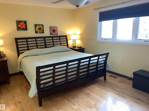 This room features light-colored hardwood flooring and a large window with blinds, providing natural light - 14212 30 Street, Edmonton, AB - Indoor Photo Showing Bedroom