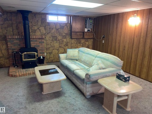Living space featuring a wood-burning stove with a brick hearth, stone-patterned wall, and wood paneling - 14212 30 Street, Edmonton, AB - Indoor Photo Showing Basement With Fireplace