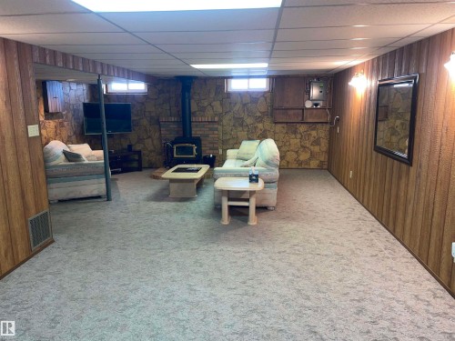 Spacious room featuring carpeted flooring, wood paneling, a stone accent wall, and a wood-burning stove - 14212 30 Street, Edmonton, AB - Indoor Photo Showing Basement