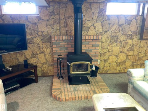 Living area featuring a freestanding black stove on a brick hearth, set against a wall with stone-look paneling and brick accents - 14212 30 Street, Edmonton, AB - Indoor With Fireplace