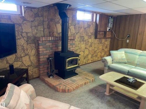 The property features a wood-burning stove with a brick hearth, set against a wall with a textured stone-like finish - 14212 30 Street, Edmonton, AB - Indoor With Fireplace