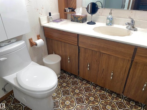Bathroom featuring a white toilet, wood-look vanity with a white countertop and an integrated sink, and patterned floor tiles - 14212 30 Street, Edmonton, AB - Indoor Photo Showing Bathroom