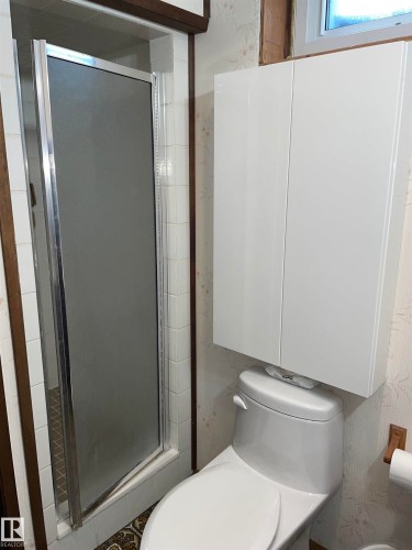 Bathroom featuring a shower with a frosted glass door, a toilet, and a wall-mounted white storage cabinet - 14212 30 Street, Edmonton, AB - Indoor Photo Showing Bathroom