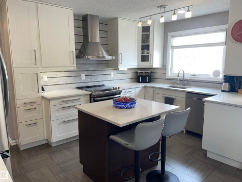 The kitchen features white cabinetry, stainless steel appliances, and a central island with a light-colored countertop - 14212 30 Street, Edmonton, AB - Indoor Photo Showing Other Room