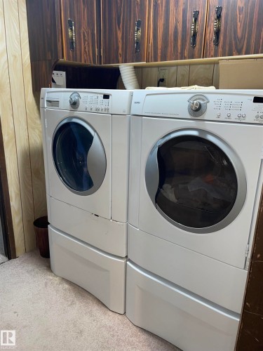This utility area features a washing machine and dryer, both in white, situated beneath dark wood-grain cabinetry with decorative brass handles - 14212 30 Street, Edmonton, AB - Indoor Photo Showing Laundry Room