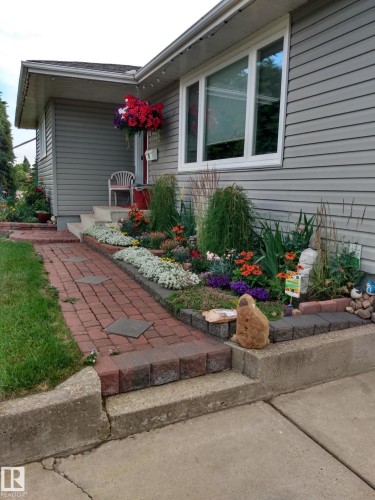 The property features grey siding, a front garden with a variety of plantings, and a red brick pathway - 14212 30 Street, Edmonton, AB - Outdoor With Exterior