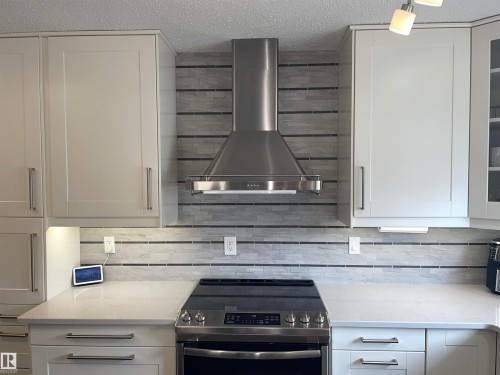 The kitchen features white cabinetry, a stainless steel range hood, and a tiled backsplash with dark accent lines - 14212 30 Street, Edmonton, AB - Indoor Photo Showing Kitchen