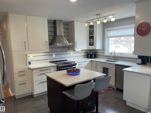 The kitchen features light-colored cabinetry, a central island with seating, stainless steel appliances, and a window with a view - 14212 30 Street, Edmonton, AB - Indoor Photo Showing Kitchen