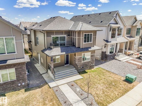 Contemporary residence featuring a dark gray shingled roof, light brown siding, and stone veneer accents - 6125 Crawford Drive, Edmonton, AB - Outdoor