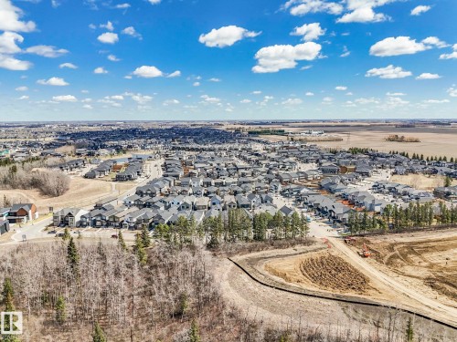 Expansive aerial showcasing a contemporary residential development with numerous single-family homes, surrounded by natural wooded areas and open fields - 6125 Crawford Drive, Edmonton, AB - Outdoor With View
