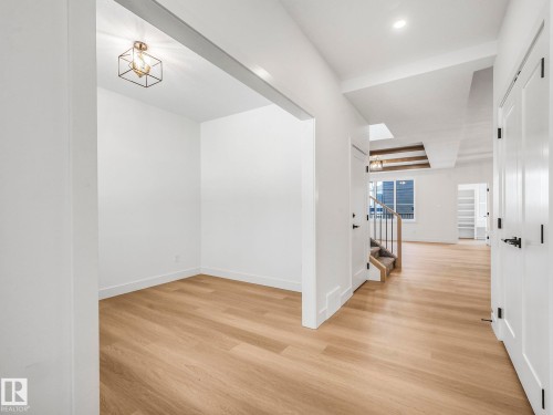 Open concept entry foyer featuring light wood-finish flooring, white walls, and a modern geometric ceiling light fixture - 6125 Crawford Drive, Edmonton, AB - Indoor Photo Showing Other Room