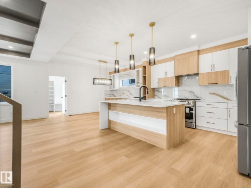Modern kitchen featuring a central island with white countertop, dual-tone cabinetry, stainless steel appliances, and a full-height marble-look backsplash - 6125 Crawford Drive, Edmonton, AB - Indoor Photo Showing Kitchen With Upgraded Kitchen