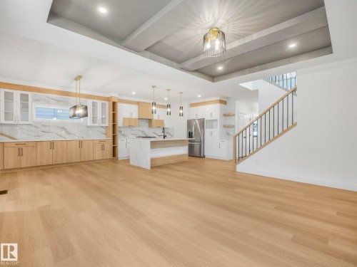 Open-concept living area featuring light wood-finish flooring, a contemporary kitchen with white and wood-tone cabinetry, a waterfall island, and integrated stainless steel appliances - 6125 Crawford Drive, Edmonton, AB - Indoor Photo Showing Kitchen