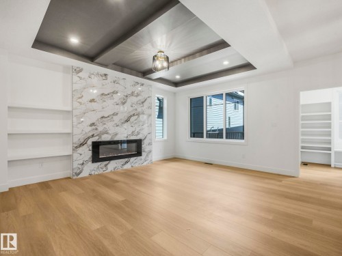 Spacious room featuring a stone-look fireplace surround, an electric fireplace insert, and built-in shelving - 6125 Crawford Drive, Edmonton, AB - Indoor Photo Showing Other Room With Fireplace