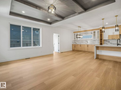 Spacious interior featuring wide-plank wood-finish flooring, a tray ceiling with recessed lighting, and a modern chandelier - 6125 Crawford Drive, Edmonton, AB - Indoor