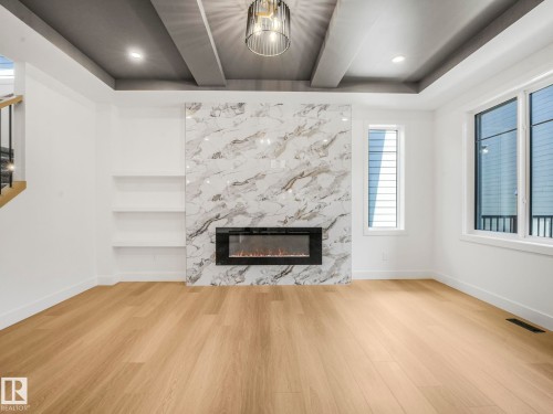 Spacious room featuring light wood-finish flooring, a contemporary electric fireplace with a floor-to-ceiling marbled surround, and built-in shelving - 6125 Crawford Drive, Edmonton, AB - Indoor Photo Showing Living Room With Fireplace