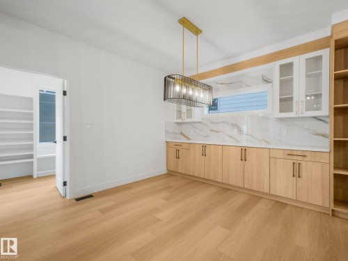 Built-in cabinetry with wood-finish bases and glass-front upper cabinets, complemented by a stone-look slab backsplash and countertops - 6125 Crawford Drive, Edmonton, AB - Indoor