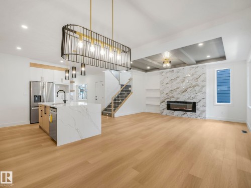 Open-concept living space featuring wood-finish flooring, a contemporary kitchen island with a waterfall countertop, and a statement fireplace with a stone-look surround - 6125 Crawford Drive, Edmonton, AB - Indoor With Fireplace
