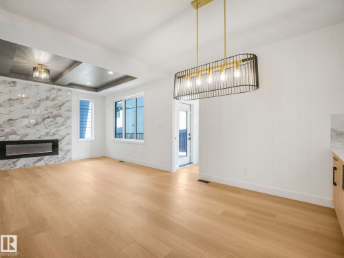 Spacious interior with wood-finish flooring, a contemporary linear fireplace with a marble-look surround, and recessed ceiling lighting - 6125 Crawford Drive, Edmonton, AB - Indoor Photo Showing Other Room With Fireplace
