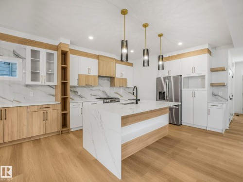 Contemporary kitchen featuring a large central island with waterfall countertop, stainless steel appliances, two-tone cabinetry, wood-finish flooring, and pendant lighting - 6125 Crawford Drive, Edmonton, AB - Indoor Photo Showing Kitchen