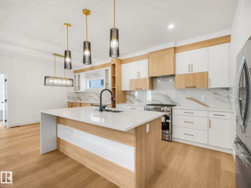 Contemporary kitchen featuring a large central island with a waterfall countertop, two-tone cabinetry, wood-finish flooring, a stainless steel range, and a full-height backsplash - 6125 Crawford Drive, Edmonton, AB - Indoor Photo Showing Kitchen With Upgraded Kitchen