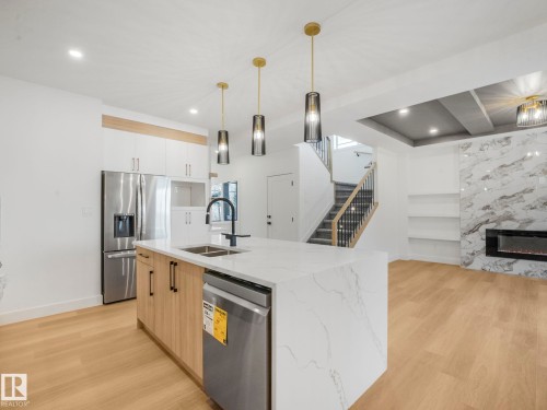 Gourmet kitchen featuring a waterfall island with a double sink and pendant lighting, stainless steel appliances, and wood-finish flooring - 6125 Crawford Drive, Edmonton, AB - Indoor Photo Showing Kitchen With Double Sink With Upgraded Kitchen