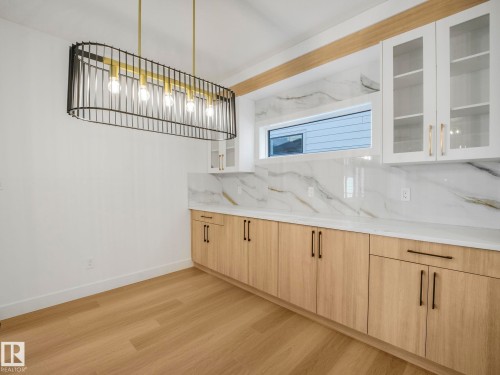 Modern linear pendant light fixture illuminates the space featuring wood-finish flooring - 6125 Crawford Drive, Edmonton, AB - Indoor